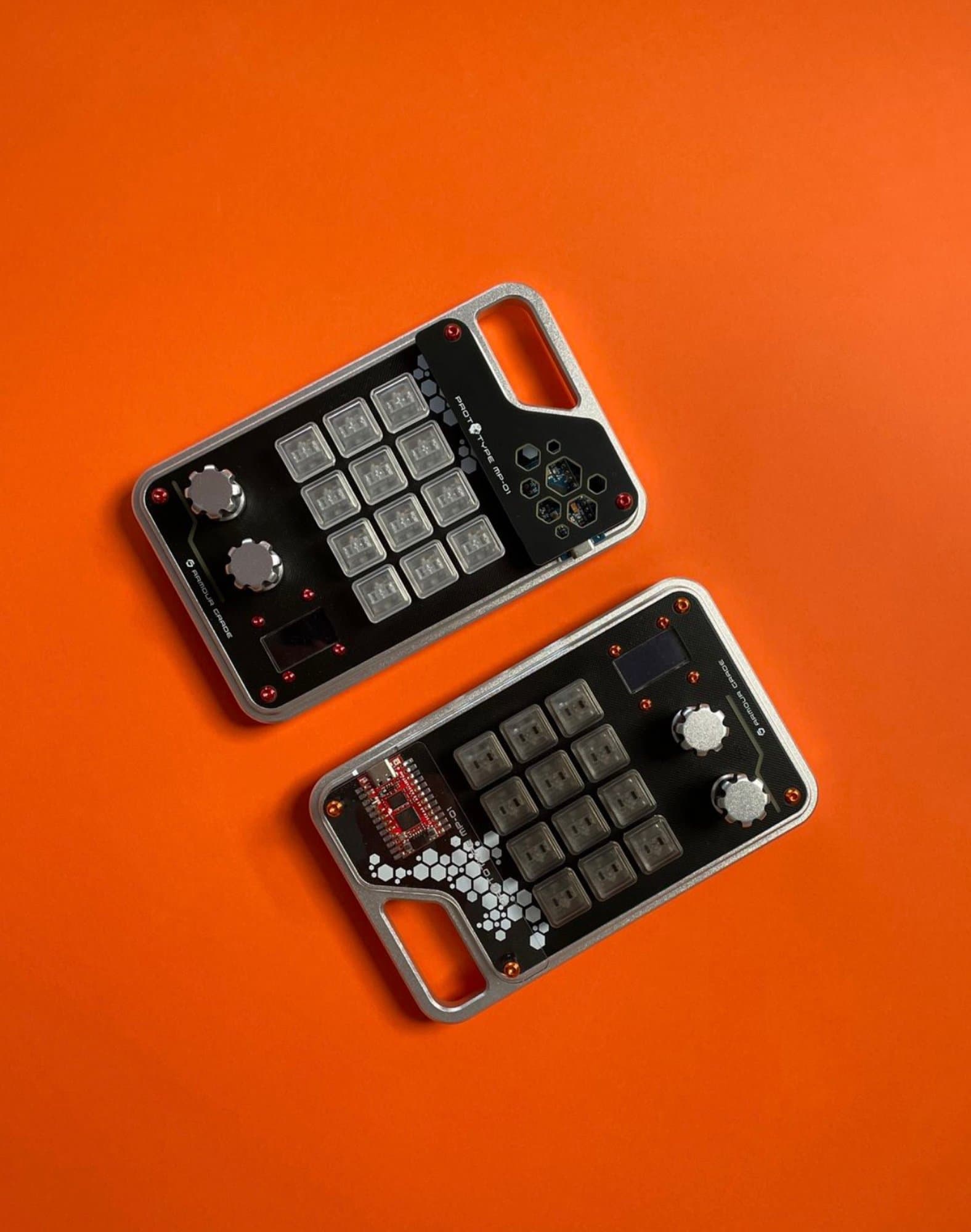 Prototype MP-01 custom mechanical macropads featuring CNC aluminum frames and rotary encoders arranged on an orange surface.