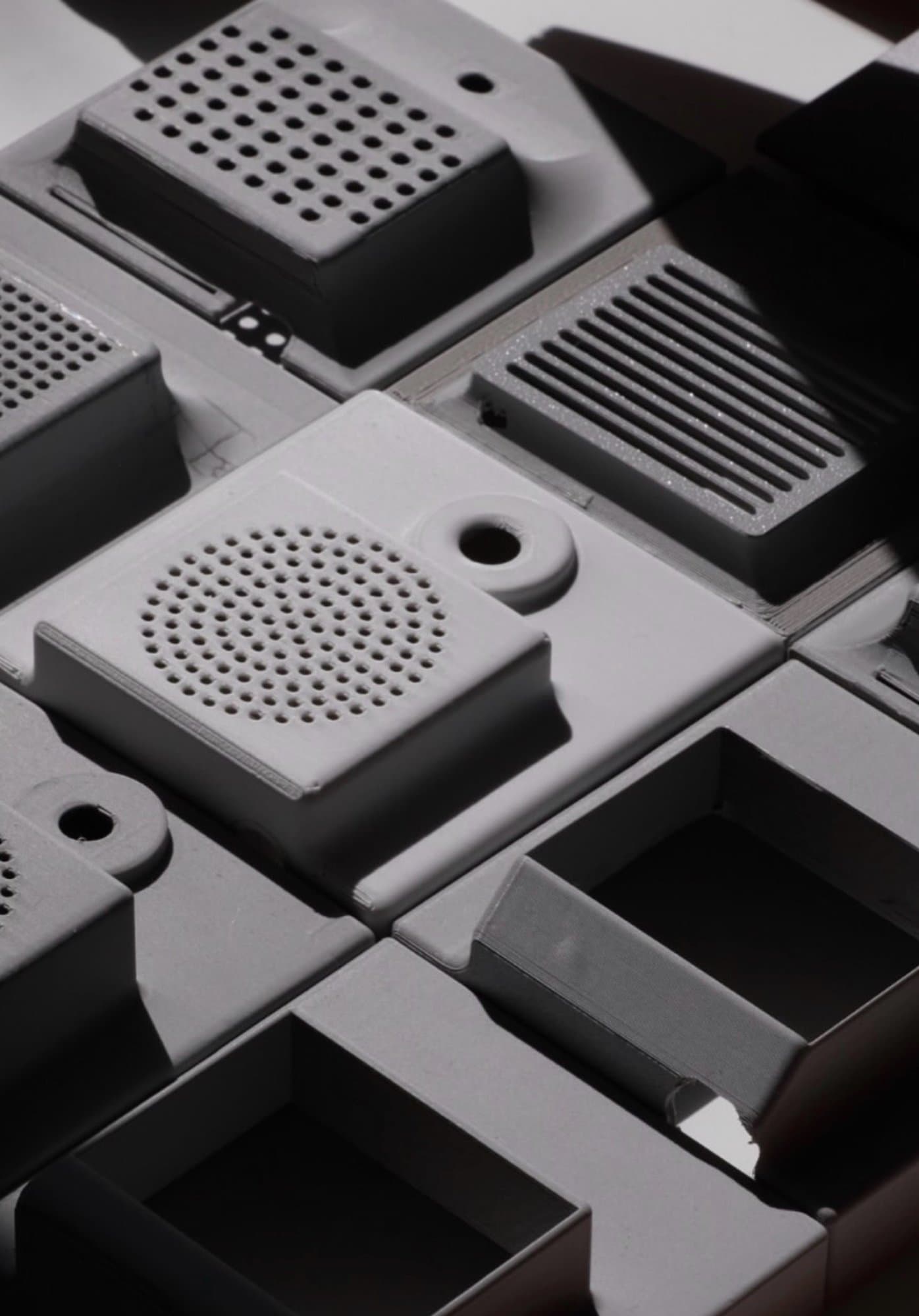 A collection of 3D-printed modular plastic components and speaker grilles arranged in an industrial design layout under dramatic lighting.