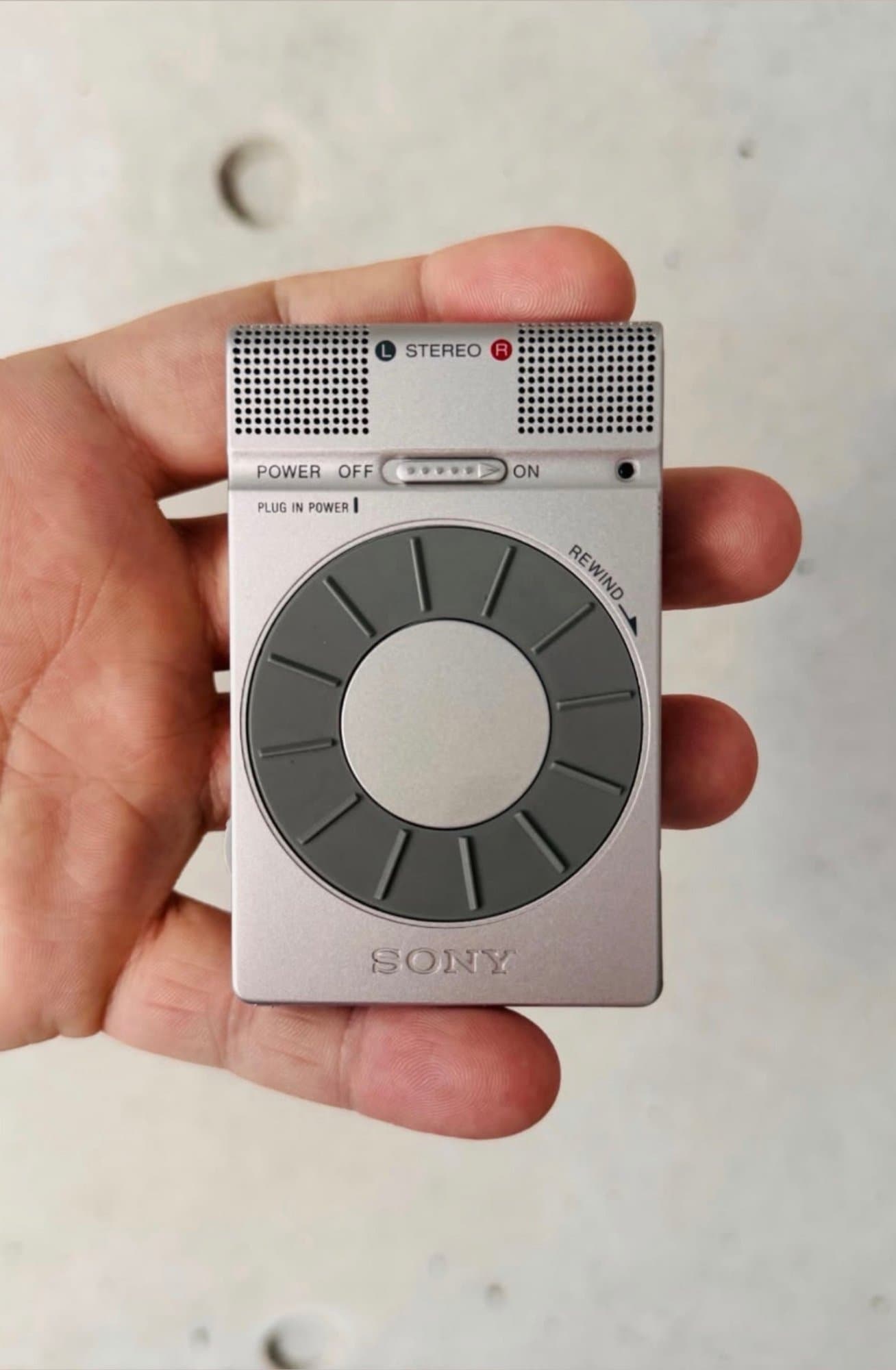 Hand holding a vintage compact Sony stereo microphone and recorder unit with a circular dial and industrial metallic finish.