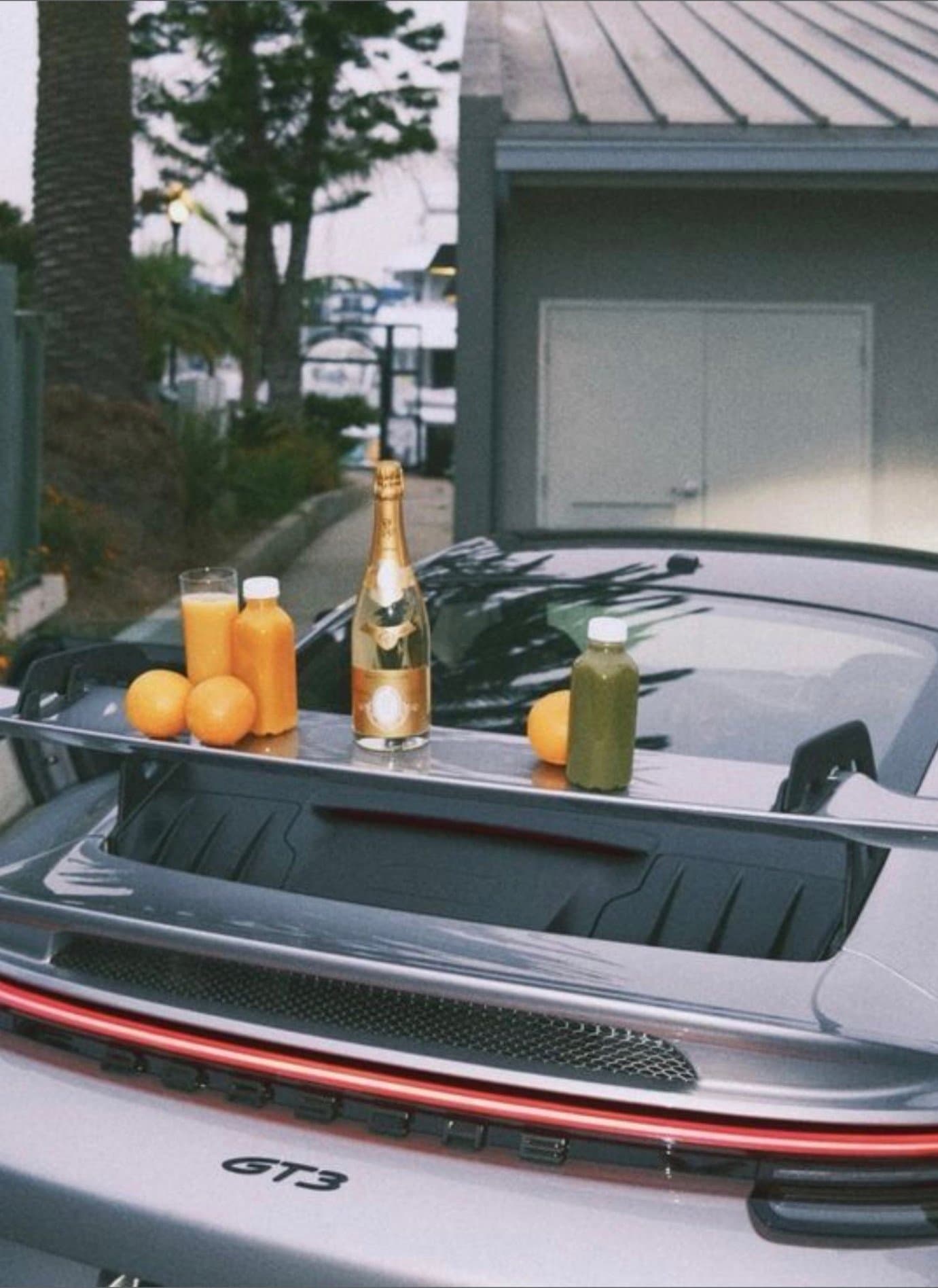 A Porsche 911 GT3 rear wing used as an impromptu breakfast table with champagne, oranges, and juice.