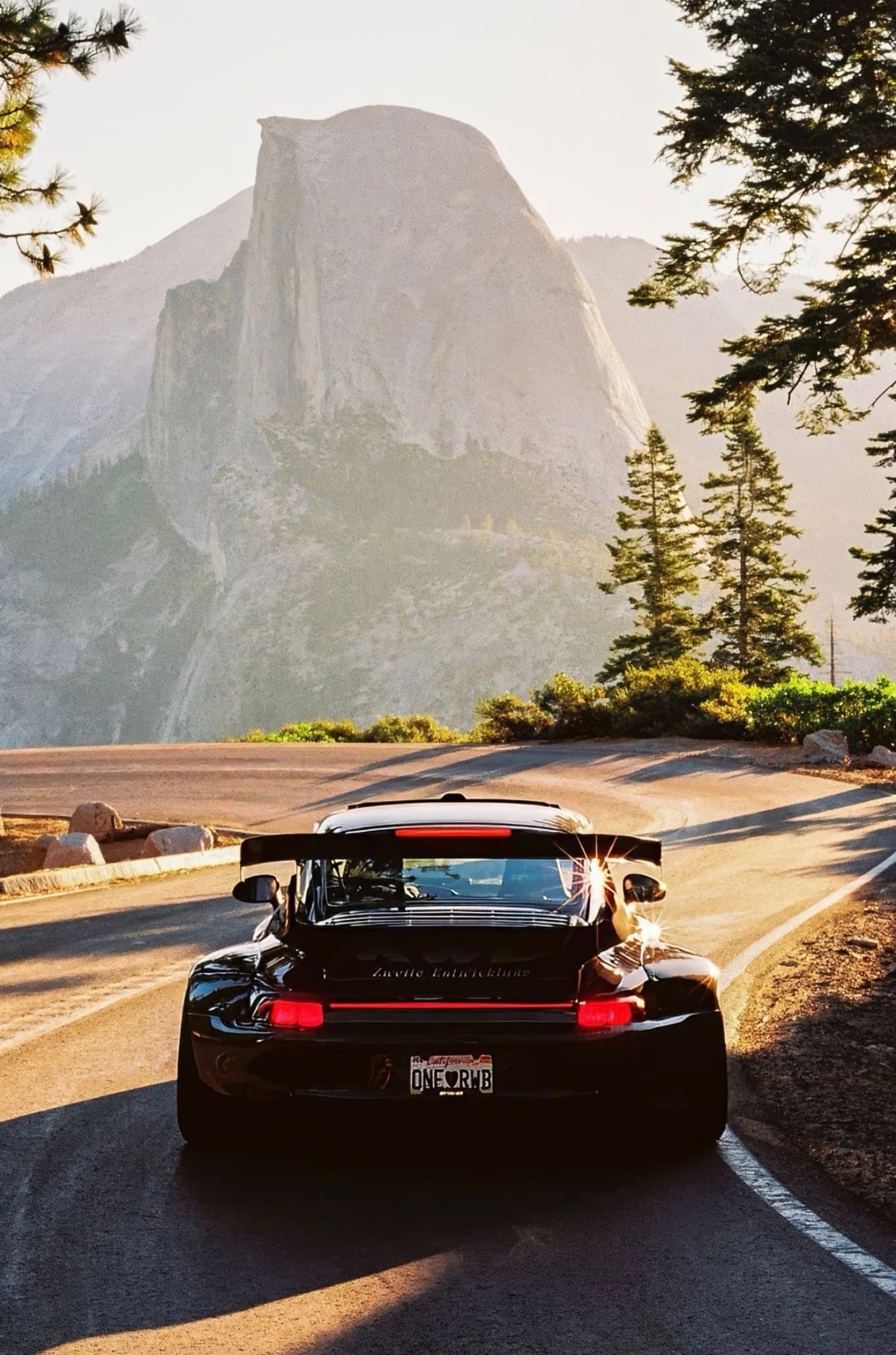 A black widebody RWB Porsche 911 drives along a winding road with Half Dome towering in the background at Yosemite National Park.